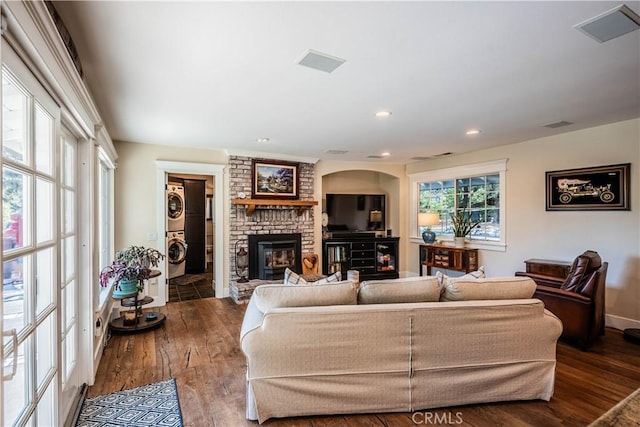 living room featuring visible vents, a brick fireplace, stacked washer / drying machine, recessed lighting, and wood finished floors