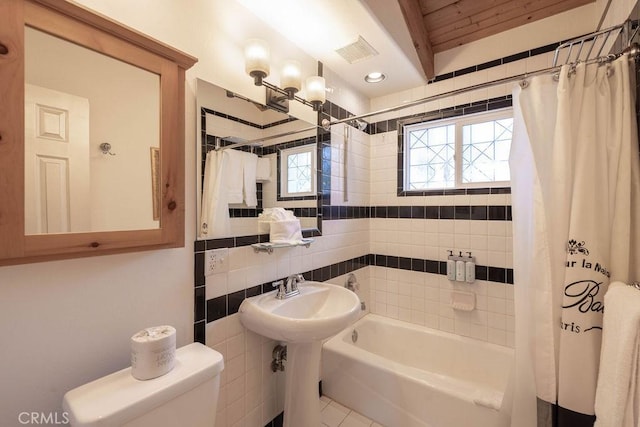 bathroom featuring tasteful backsplash, visible vents, toilet, shower / tub combo with curtain, and tile walls