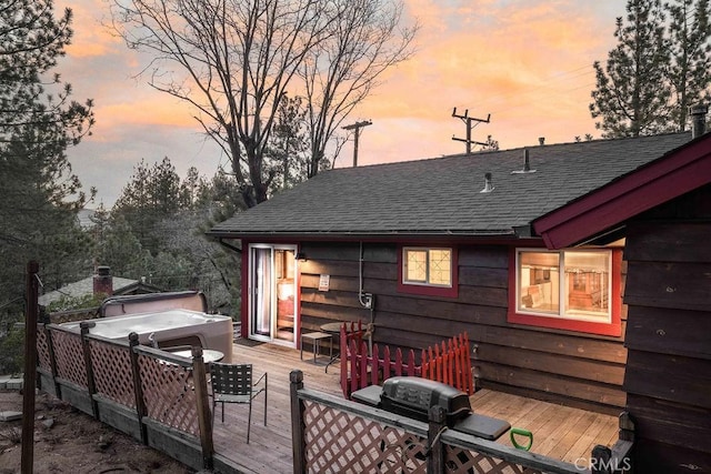 back of property at dusk with a shingled roof and a wooden deck
