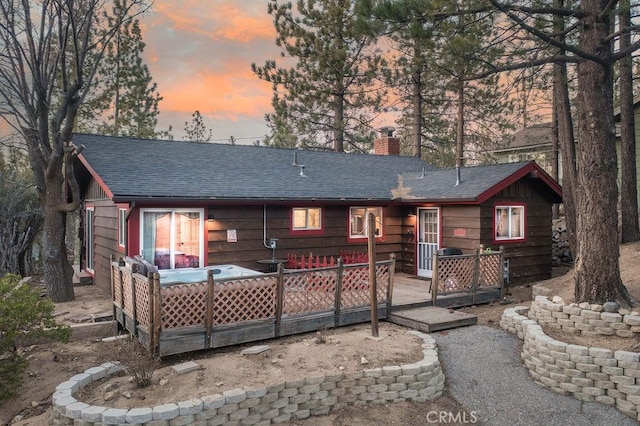 back of property at dusk featuring a deck, a chimney, and a shingled roof