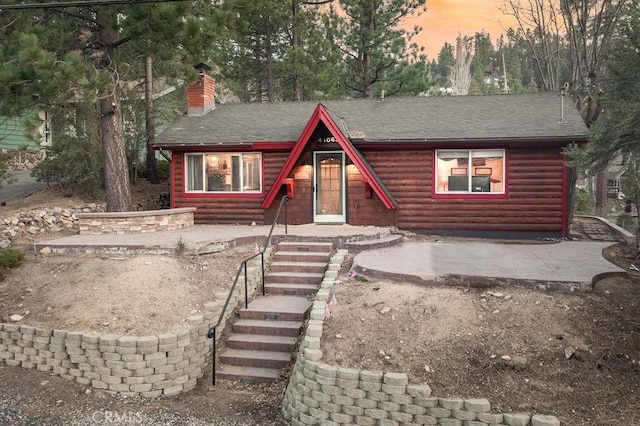 view of front of home featuring roof with shingles, a chimney, and faux log siding