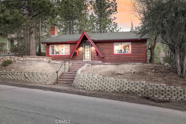 log cabin featuring roof with shingles, a chimney, and faux log siding