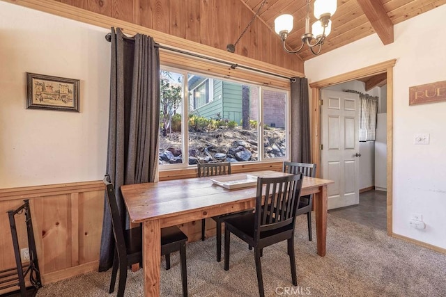 carpeted dining space with a chandelier, wooden ceiling, wainscoting, wooden walls, and beam ceiling