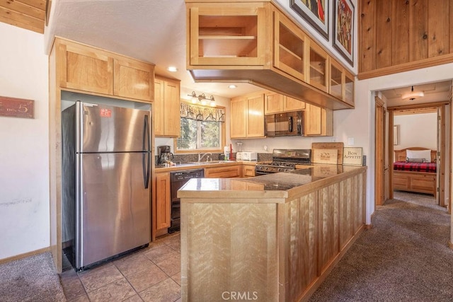kitchen featuring light brown cabinets, a peninsula, glass insert cabinets, black appliances, and a sink