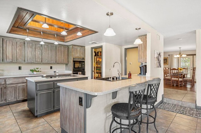 kitchen featuring a kitchen breakfast bar, light countertops, a sink, light tile patterned floors, and black appliances