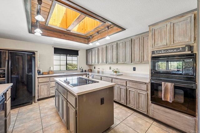 kitchen with a center island with sink, light countertops, light tile patterned floors, black appliances, and a tray ceiling