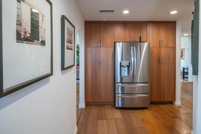 kitchen with baseboards, light wood-type flooring, stainless steel fridge, visible vents, and brown cabinetry
