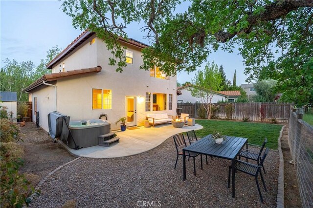 back of house with a hot tub, a fenced backyard, a tile roof, an outdoor living space, and a patio