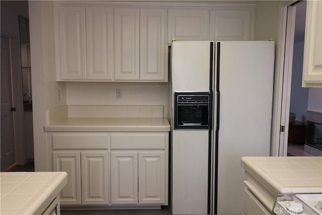 kitchen with tile counters, white refrigerator with ice dispenser, and white cabinetry