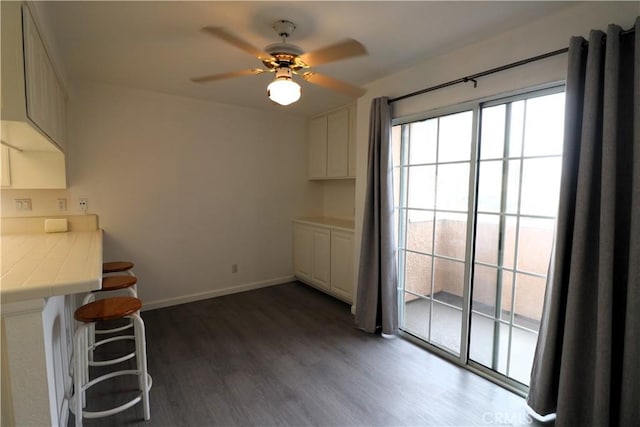 unfurnished dining area featuring baseboards, a ceiling fan, and wood finished floors