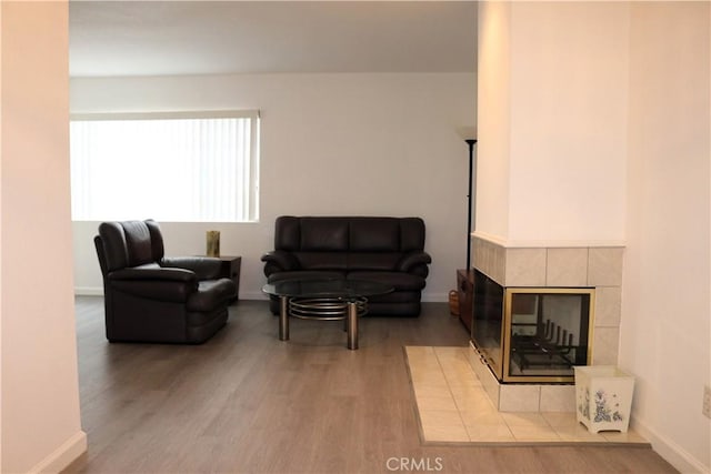 living room with a tiled fireplace, baseboards, and wood finished floors