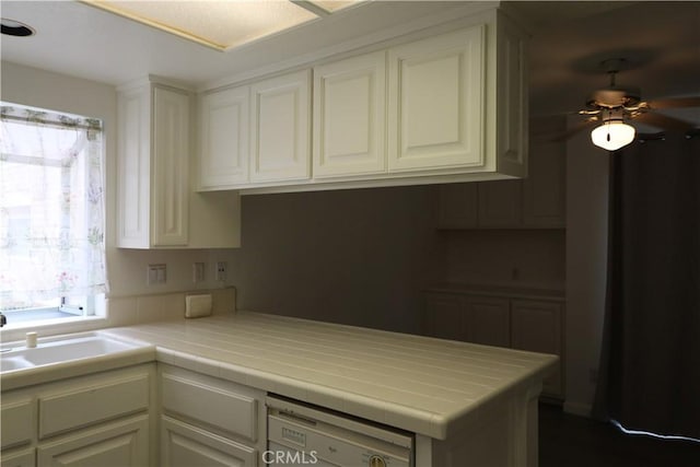 kitchen featuring a ceiling fan, tile countertops, white cabinets, a peninsula, and dishwashing machine