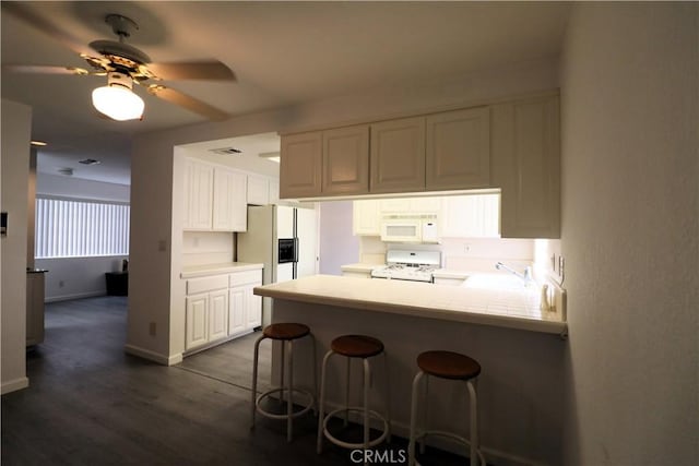 kitchen featuring ceiling fan, white cabinets, a peninsula, white appliances, and dark wood-type flooring