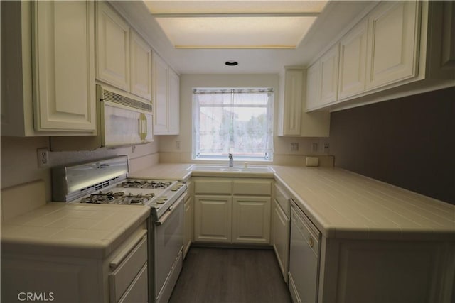 kitchen with dark wood-style flooring, a sink, white appliances, tile countertops, and a peninsula