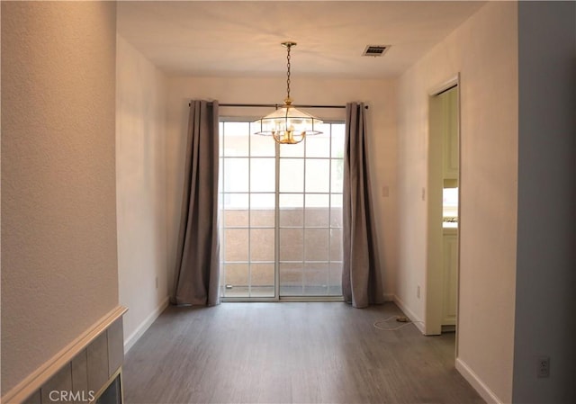 spare room with baseboards, a chandelier, wood finished floors, and visible vents