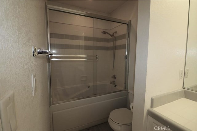 bathroom with toilet, a textured wall, enclosed tub / shower combo, and vanity