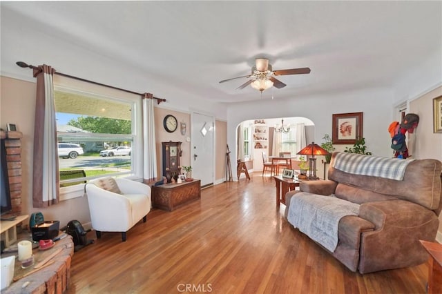living area featuring arched walkways, ceiling fan with notable chandelier, and light wood finished floors