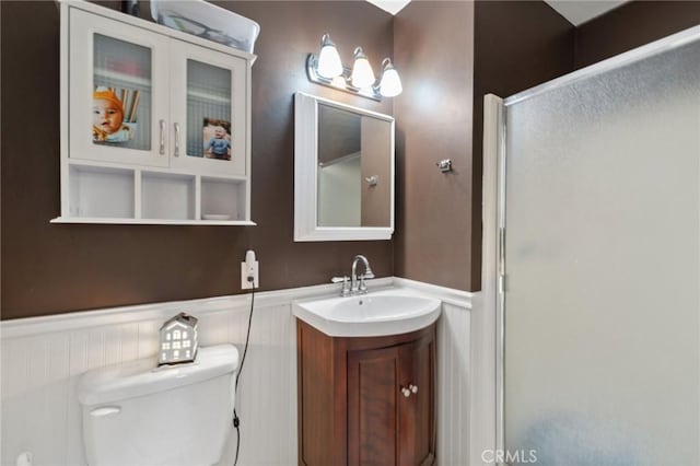 bathroom featuring vanity, a wainscoted wall, a shower stall, and toilet