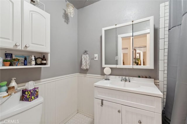 full bath featuring toilet, wainscoting, and vanity