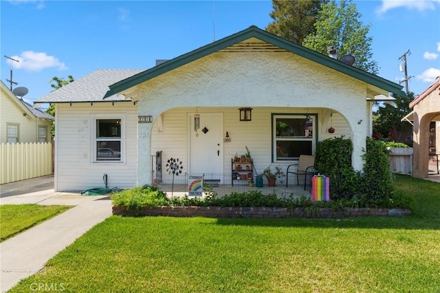 bungalow-style house with fence, covered porch, and a front yard