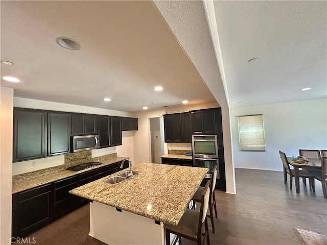 6974 Canterra Way, Fontana, CA 92336 - kitchen with appliances with stainless steel finishes, recessed lighting, an island with sink, light stone counters, and dark cabinets