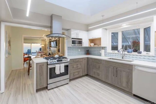 kitchen with light wood-type flooring, island range hood, decorative backsplash, stainless steel appliances, and a sink