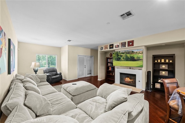 living room with visible vents, a glass covered fireplace, and dark wood finished floors