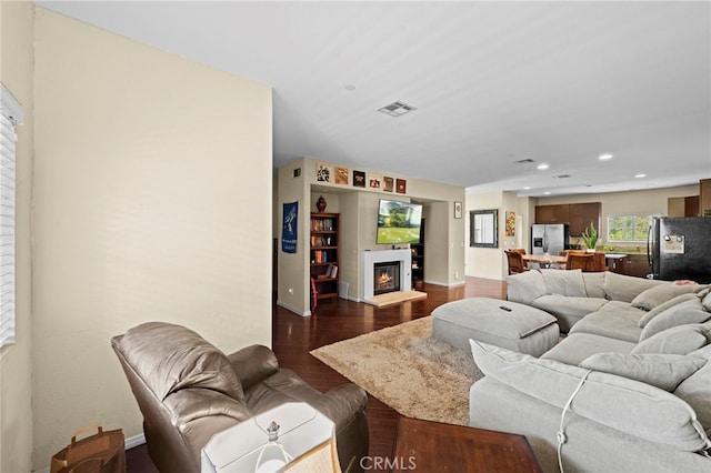 living area featuring visible vents, a glass covered fireplace, baseboards, dark wood-type flooring, and recessed lighting