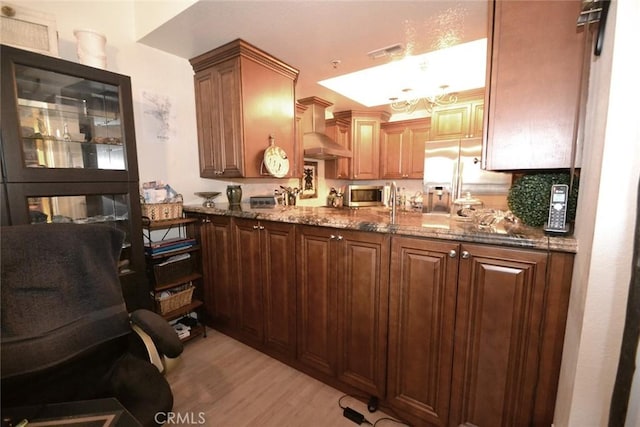 kitchen with wall chimney exhaust hood, stone counters, visible vents, stainless steel appliances, and light wood finished floors