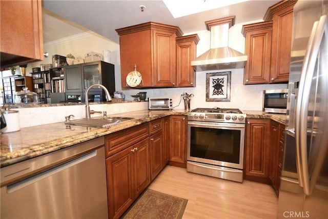 kitchen featuring light wood-style floors, wall chimney exhaust hood, a sink, stainless steel appliances, and brown cabinets