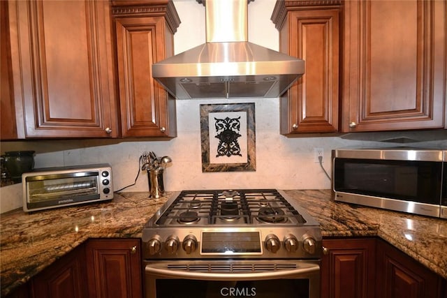 kitchen with tasteful backsplash, dark stone countertops, wall chimney range hood, stainless steel appliances, and a toaster