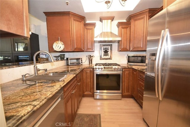 kitchen with stainless steel appliances, brown cabinetry, wall chimney exhaust hood, and a sink