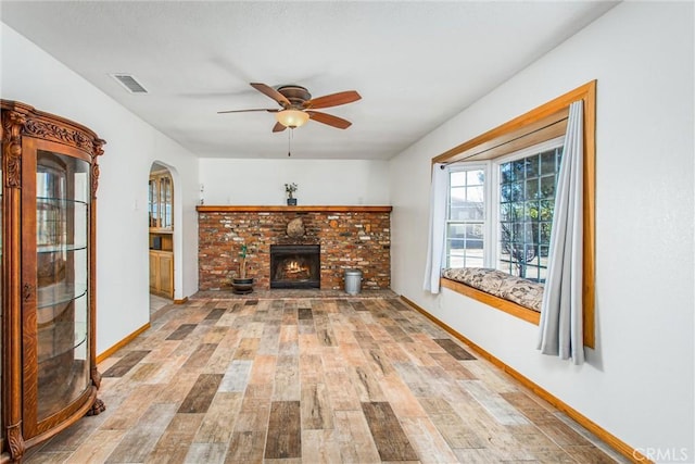 7045 Oak Hill Rd, Oak Hills, CA 92344 - unfurnished living room with ceiling fan, light wood-type flooring, visible vents, a brick fireplace, and baseboards