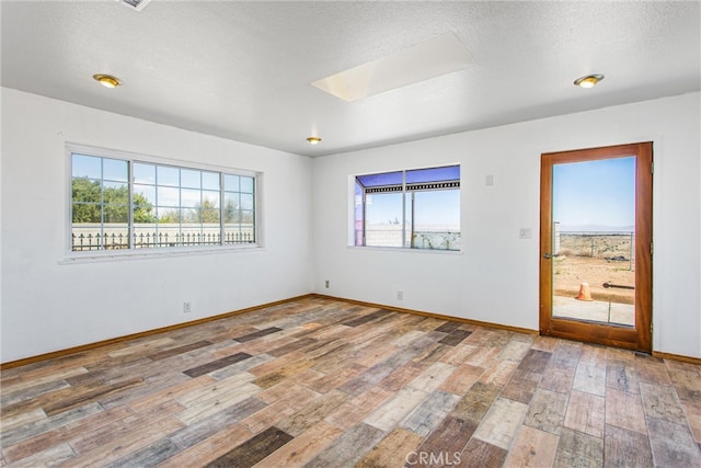 7045 Oak Hill Rd, Oak Hills, CA 92344 - unfurnished room featuring a skylight, hardwood / wood-style floors, baseboards, and a textured ceiling