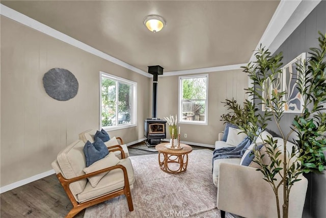 living room with crown molding, wood finished floors, a wood stove, and baseboards