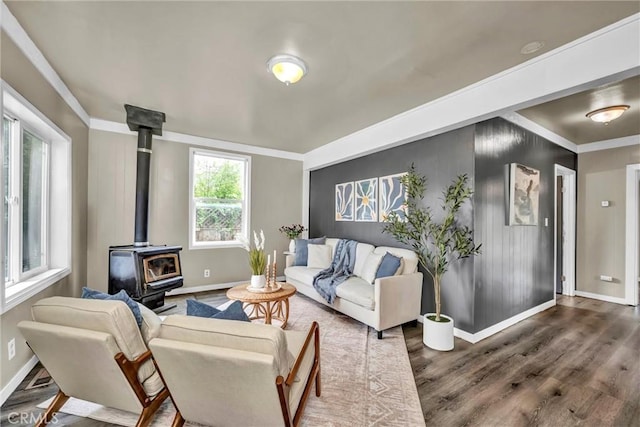 living area featuring crown molding, wood finished floors, a wood stove, and baseboards