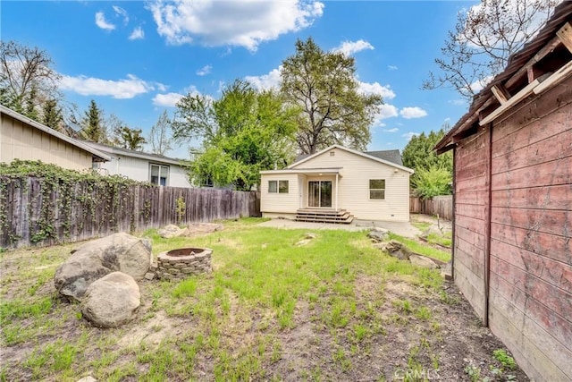 rear view of house with a fenced backyard, a fire pit, and a lawn