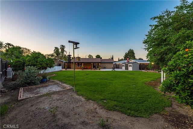 yard at dusk featuring a fenced backyard, an outbuilding, a patio, and a storage shed
