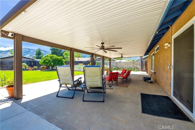 view of patio with outdoor dining space, a fenced backyard, ceiling fan, and a mountain view