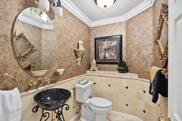 half bath featuring wallpapered walls, a wainscoted wall, toilet, a sink, and crown molding