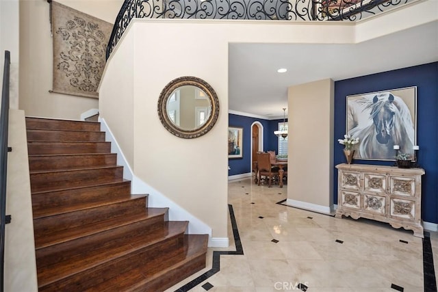 foyer entrance with arched walkways, baseboards, a chandelier, stairway, and ornamental molding