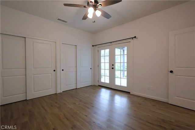 unfurnished bedroom featuring multiple closets, access to exterior, visible vents, baseboards, and wood finished floors
