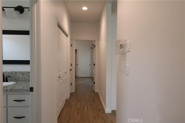 hall with recessed lighting, a sink, light wood-style flooring, and baseboards