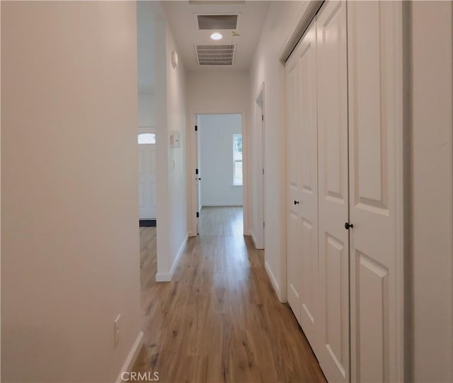 hallway featuring visible vents, light wood-style flooring, and baseboards