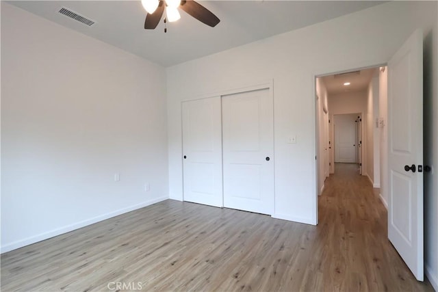 unfurnished bedroom featuring light wood-style flooring, a closet, baseboards, visible vents, and a ceiling fan