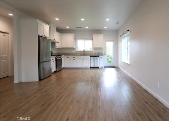 kitchen with appliances with stainless steel finishes, wood finished floors, white cabinetry, and a sink