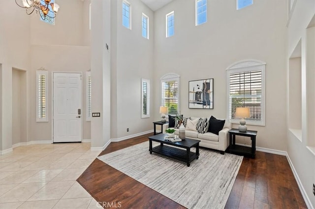living area featuring a towering ceiling, tile patterned flooring, baseboards, and a notable chandelier