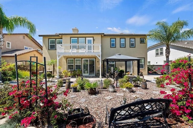 rear view of house with a balcony, stucco siding, a chimney, a patio area, and a gazebo