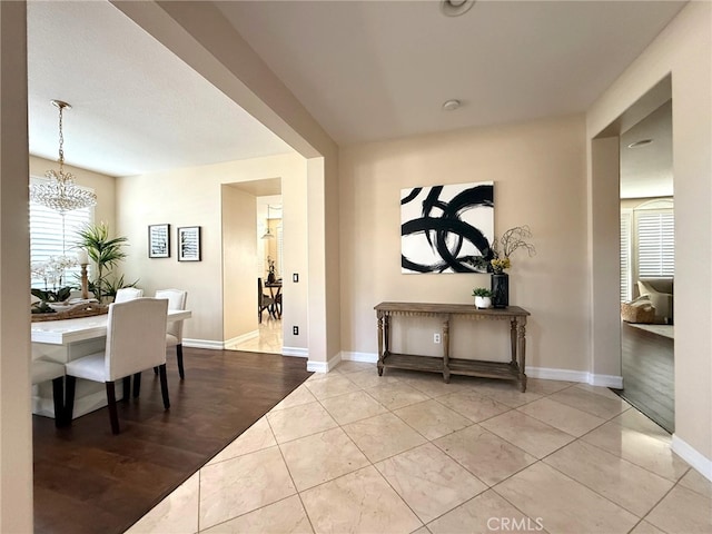 hall with tile patterned floors, baseboards, and a chandelier