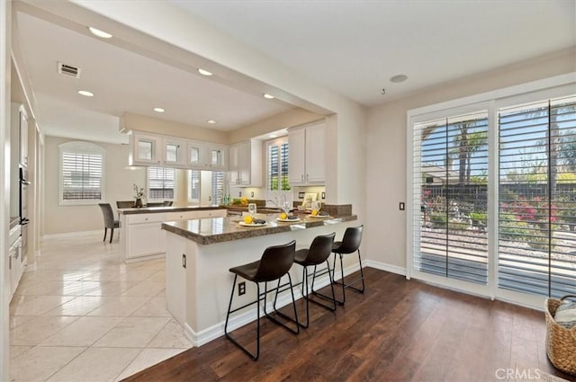 kitchen with a peninsula, white cabinetry, visible vents, wall oven, and baseboards